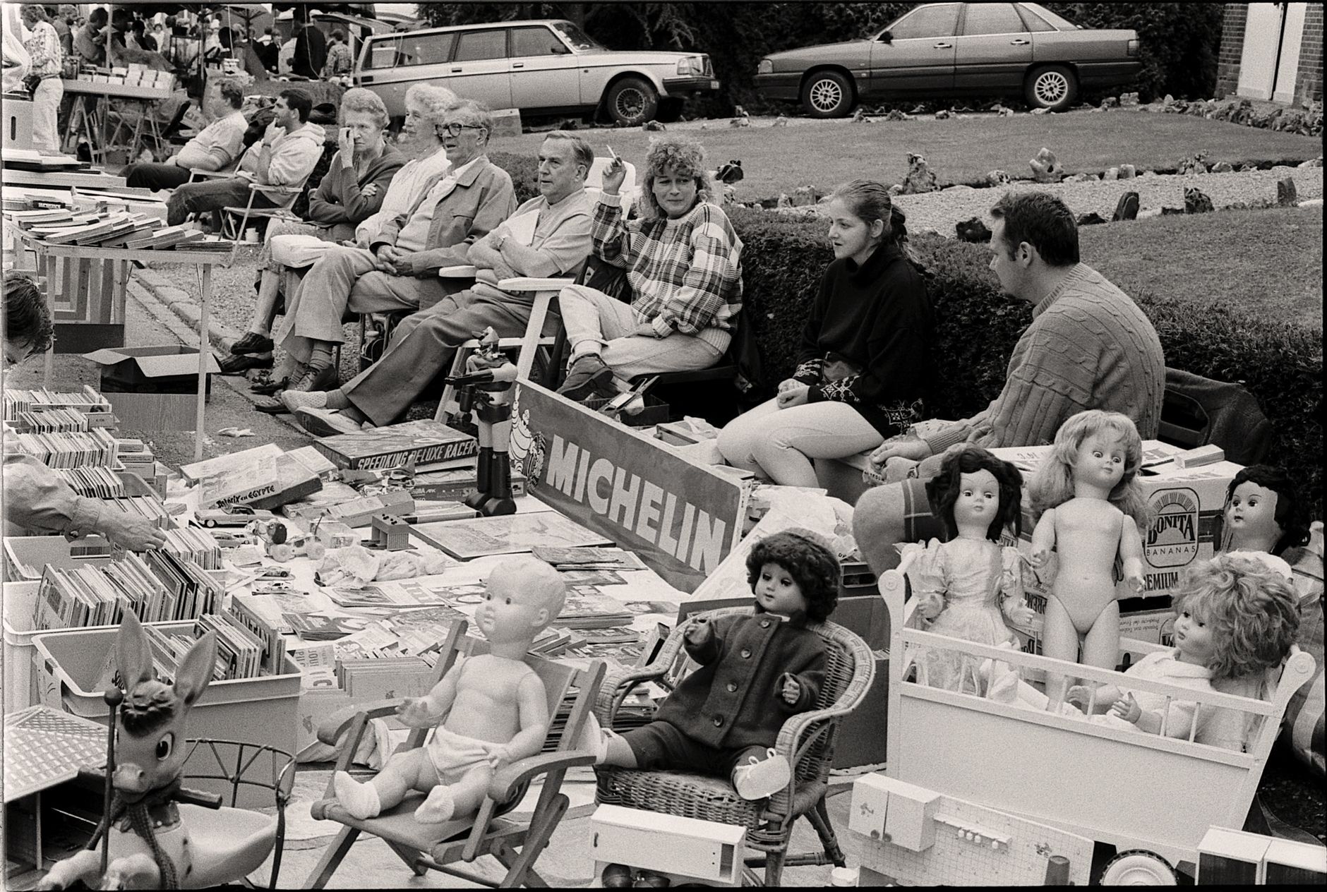 Black and white photo of a suburban garage sale showcasing vintage toys and collectibles.