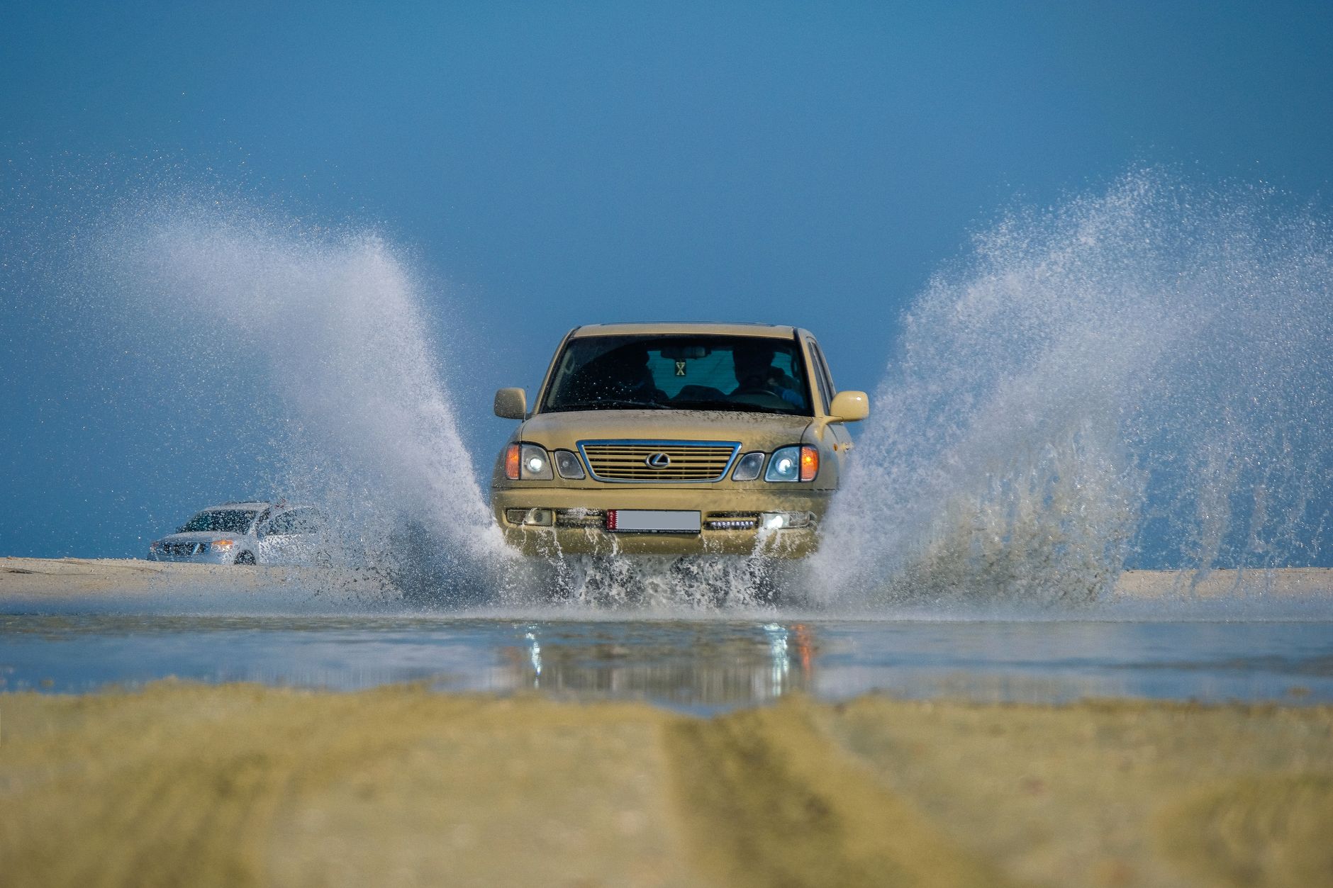 Dynamic shot of a Lexus SUV driving through water, creating a splash on a sunny outdoor day.