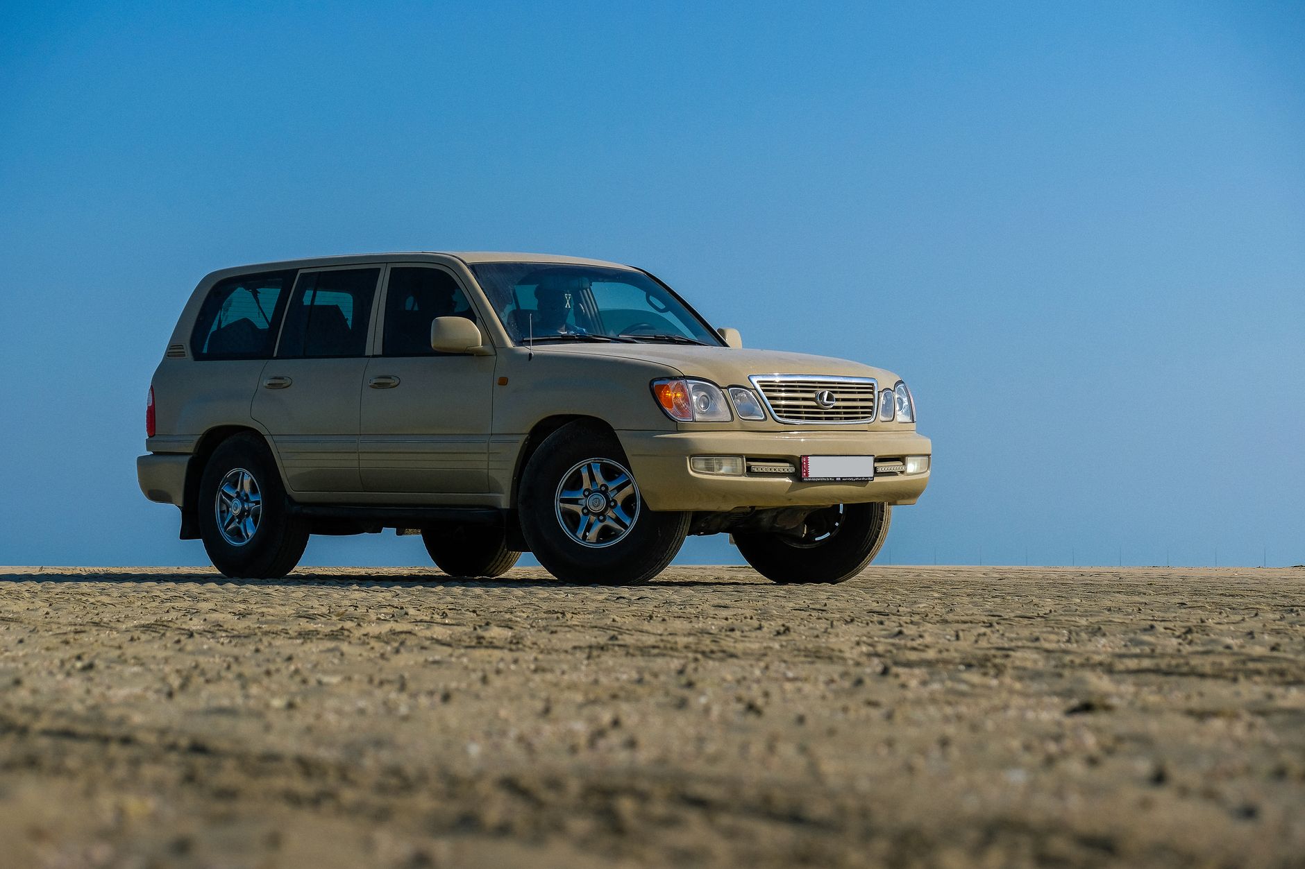 A beige SUV parked on a desert terrain under a clear blue sky.