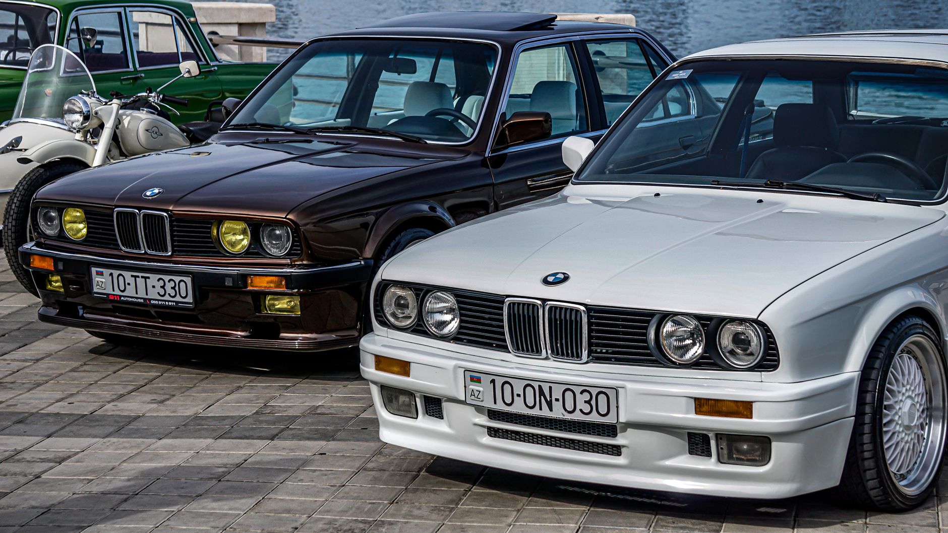 Vintage BMW cars parked by the water, showcasing classic automotive design.