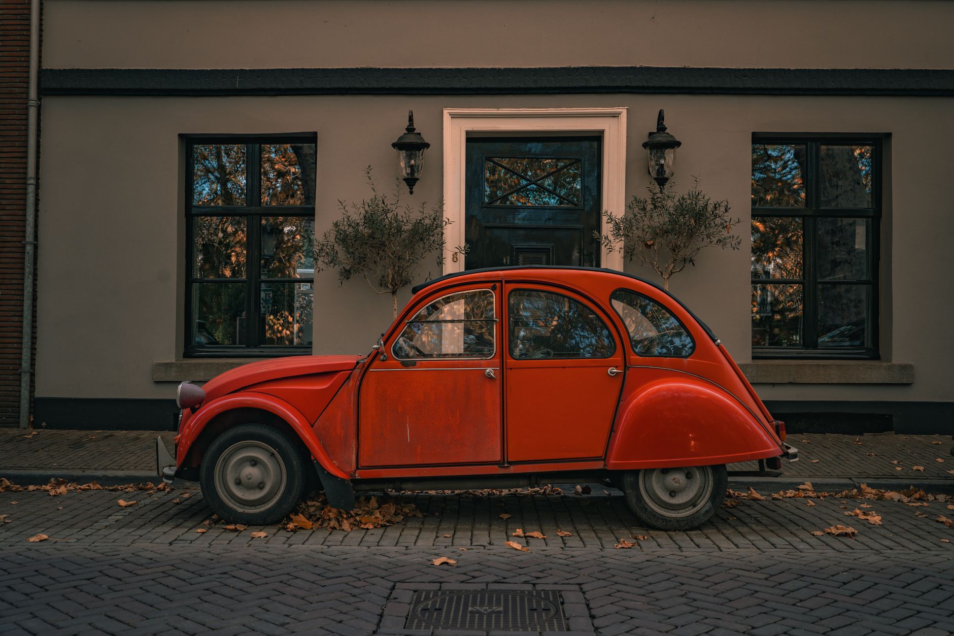 A classic red vintage car parked in front of a charming building surrounded by autumn leaves.