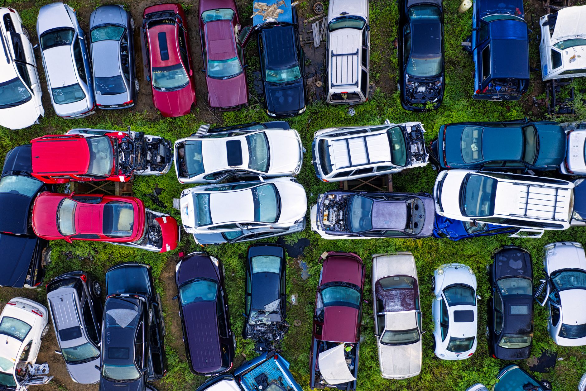 High-angle shot of various damaged cars in a junkyard surrounded by greenery.
