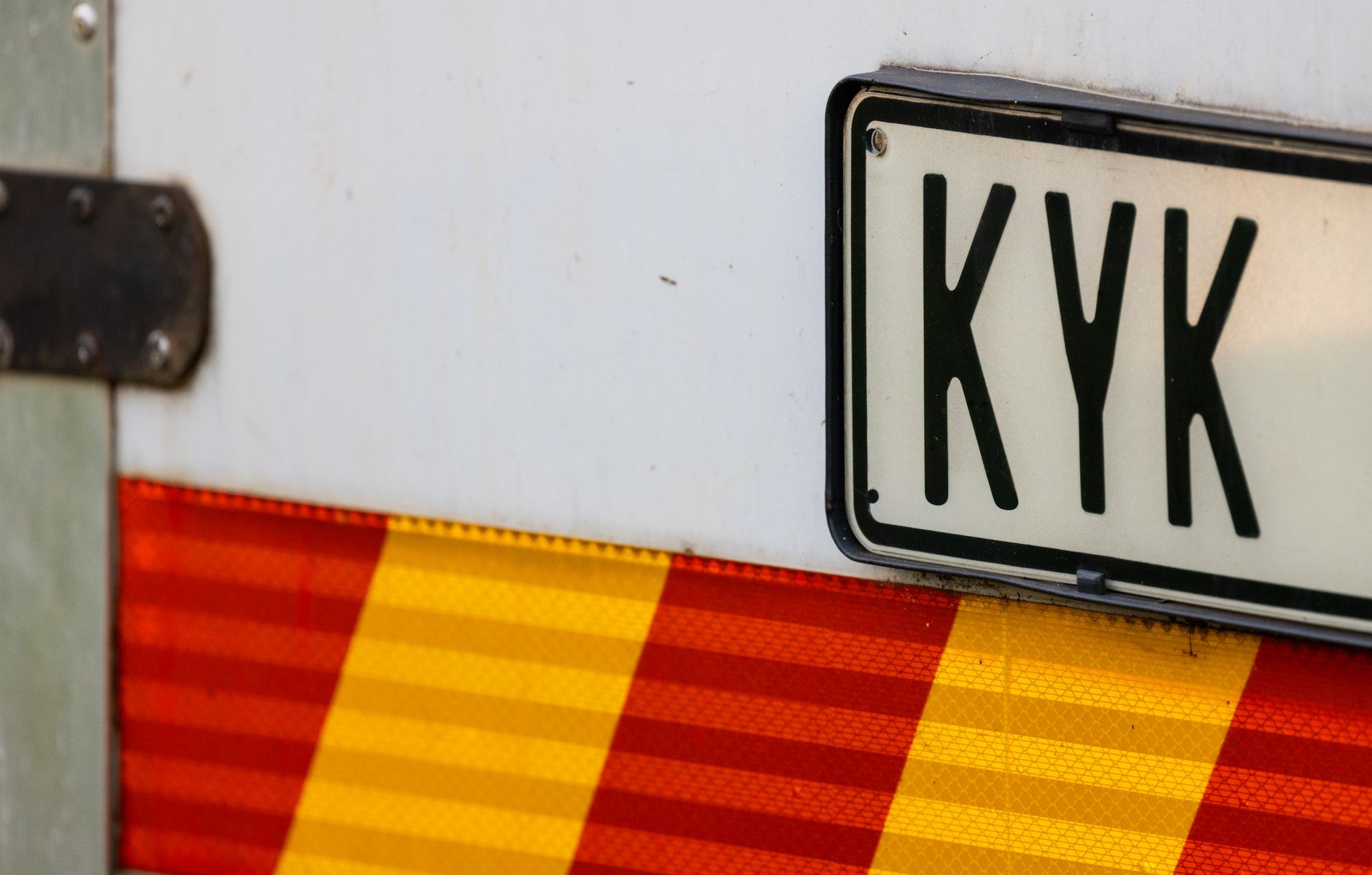 A close-up view of a vehicle's license plate with a reflective red and yellow strip.
