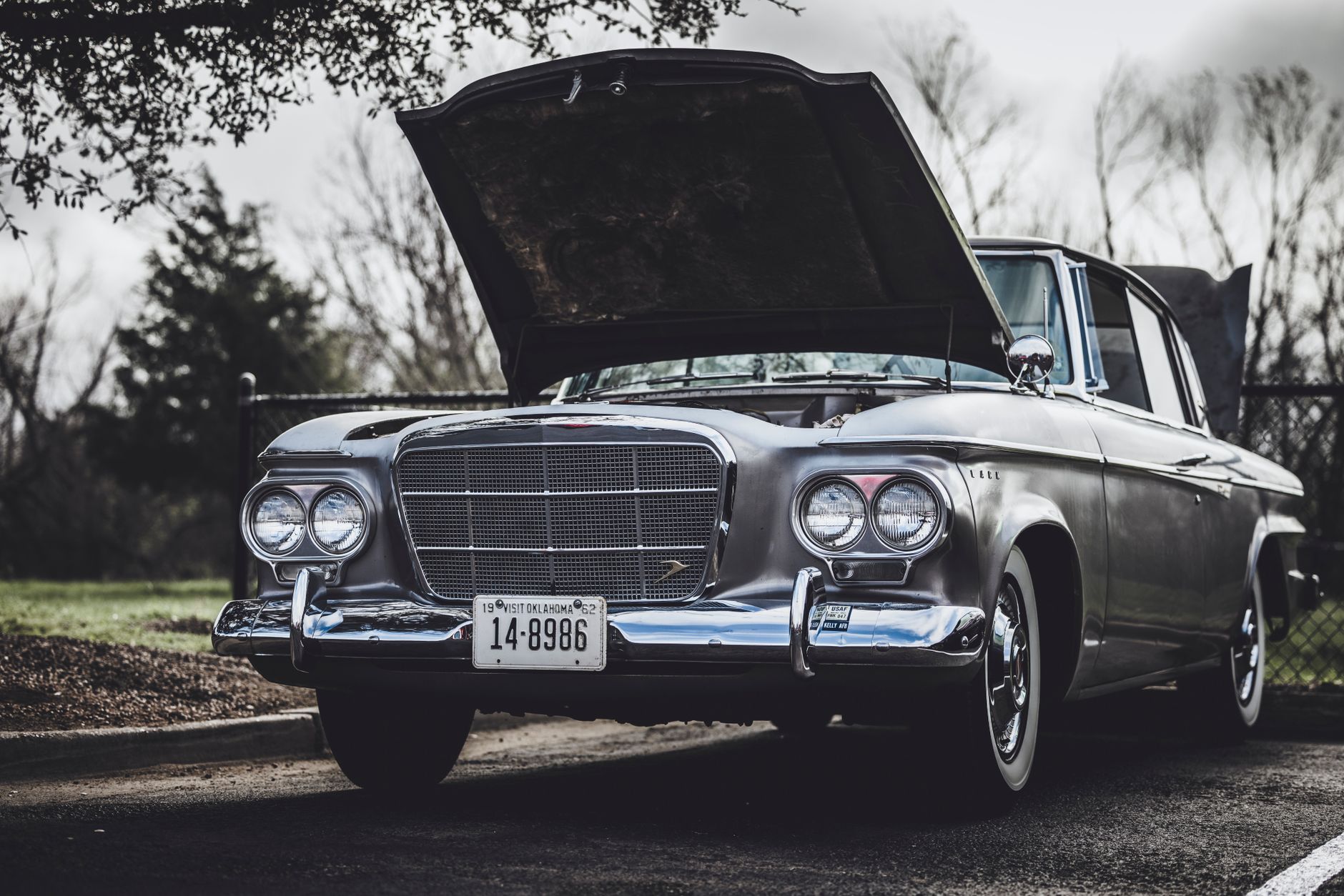 Classic silver Studebaker car with open hood displayed outdoors on a cloudy day.