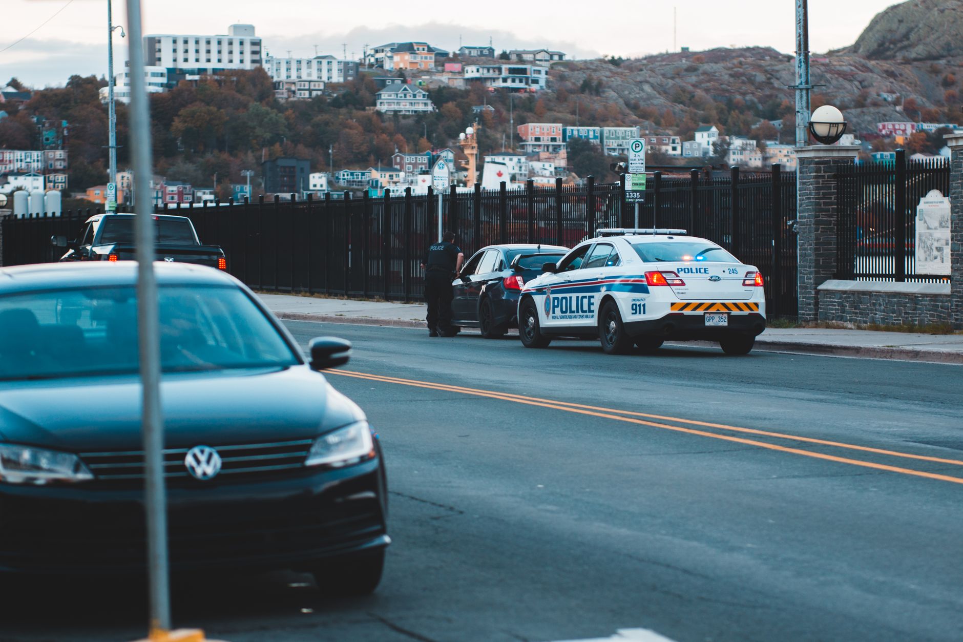 Police car parked on asphalt road near modern vehicles in city district in evening