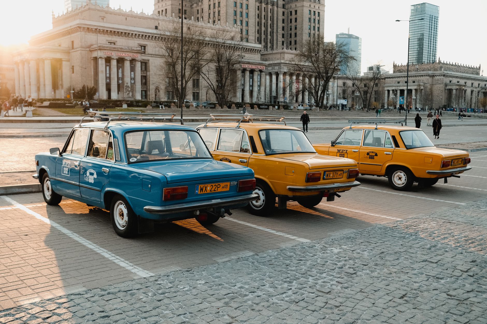 Classic cars in Warsaw at sunset near iconic Palace of Culture and Science.