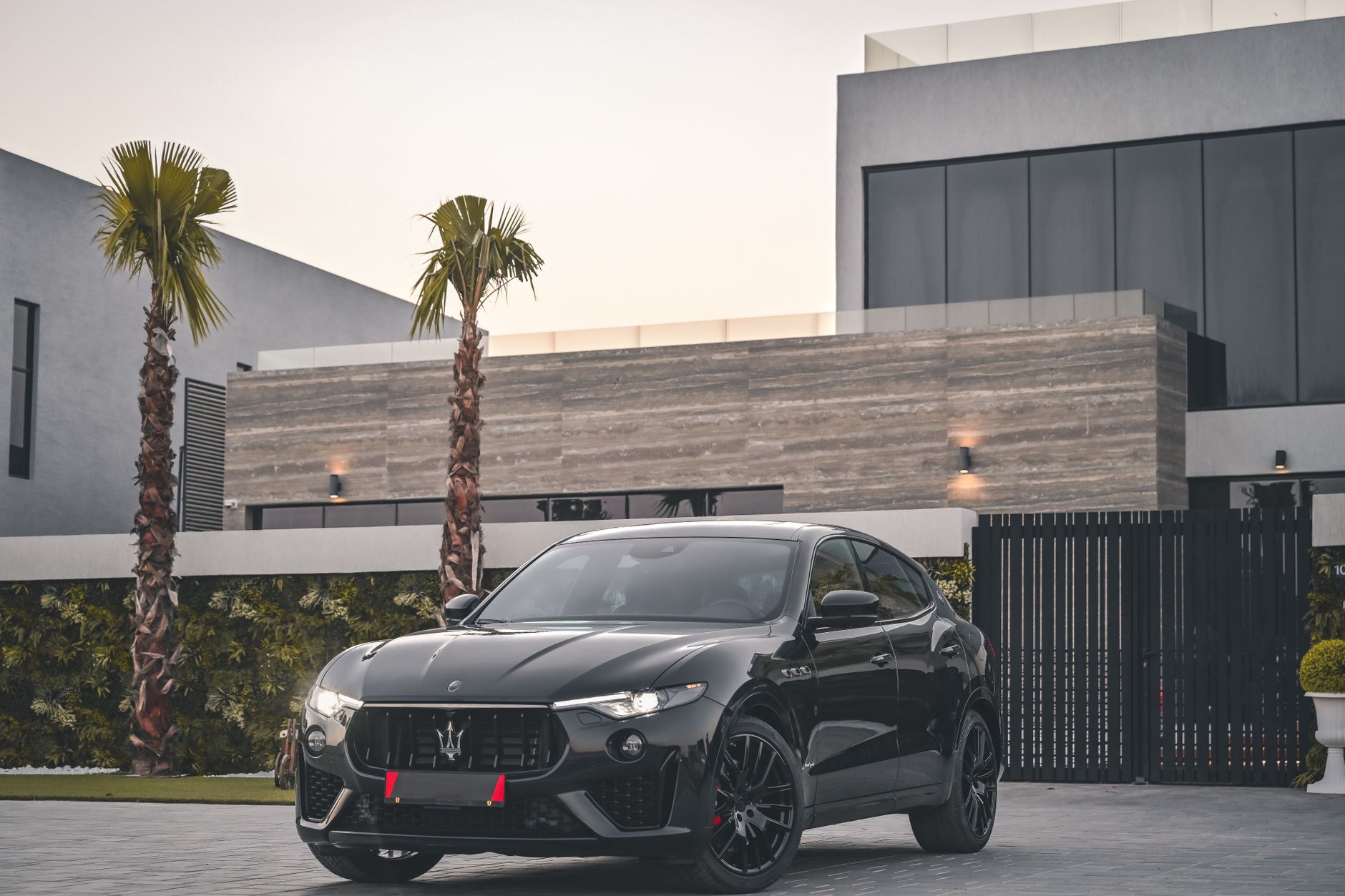 Black Maserati SUV parked in front of a modern concrete house with palm trees.