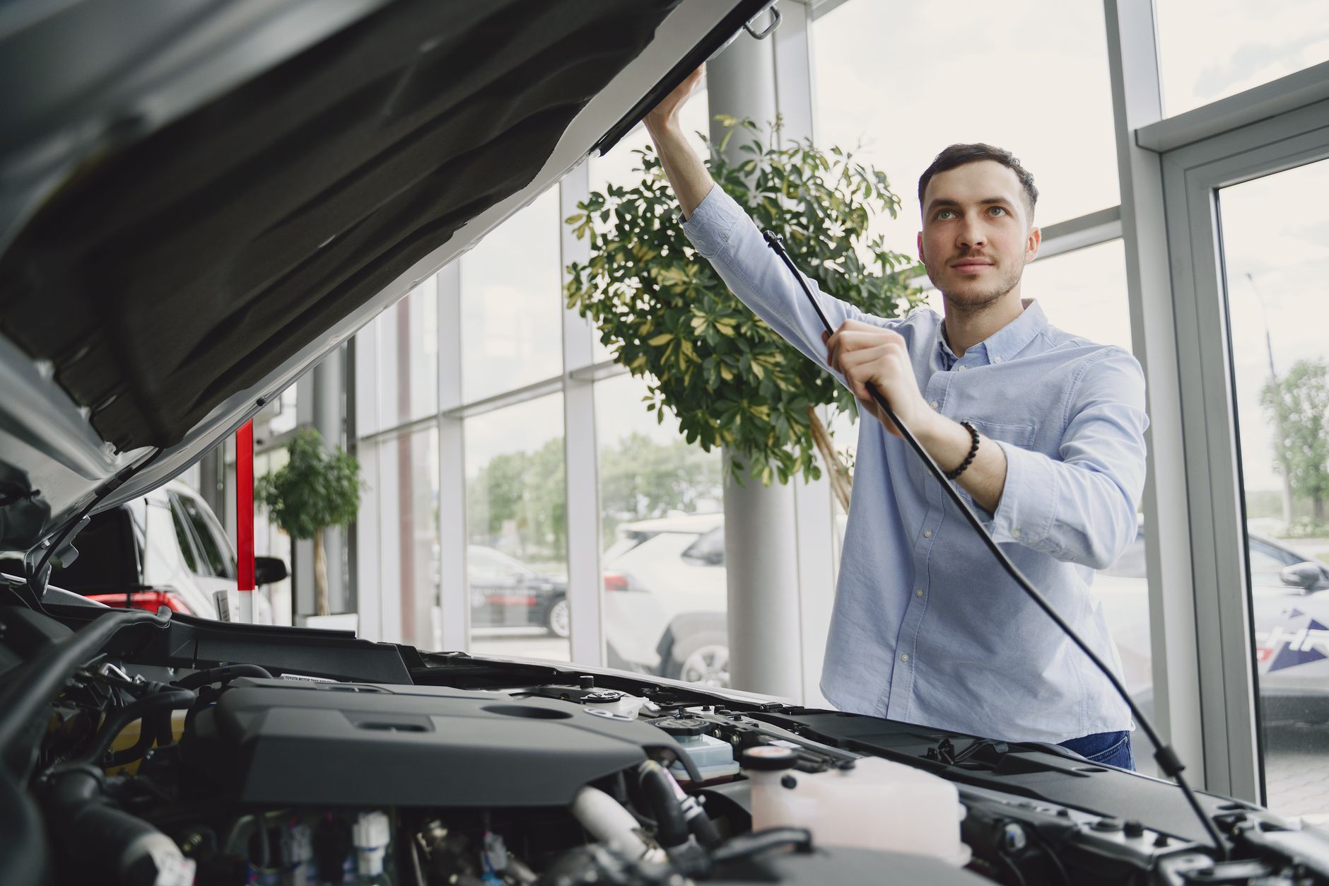 A man carefully checking a car engine in a bright, modern car showroom.