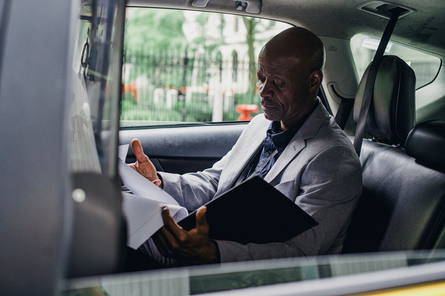Side view of African American male in elegant suit checking folder of documents in automobile