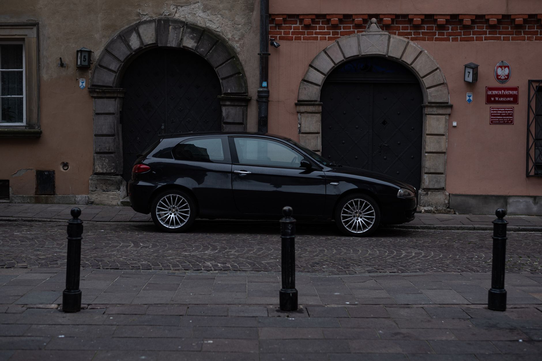 A black Alfa Romeo 147 parked in front of traditional architecture on a cobblestone street.