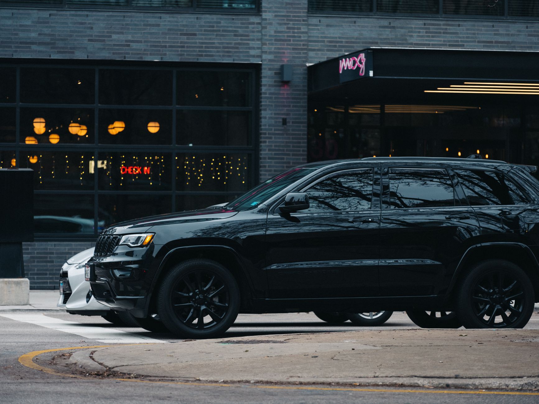 A sleek black SUV parked on a city street with modern buildings and outdoor lighting.